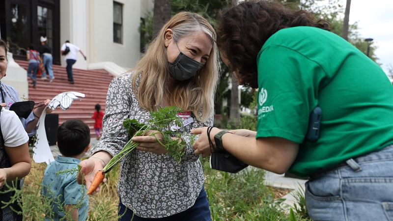 Una monitora enseña una planta a una mujer y una niña en un huerto